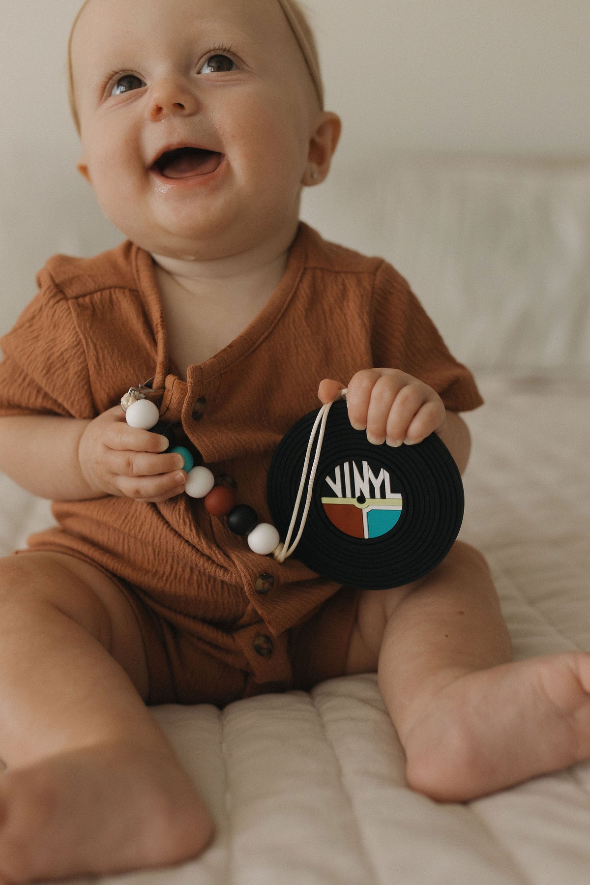 Happy baby holding a vinyl record silicone baby teether with clip, showcasing the stylish design.