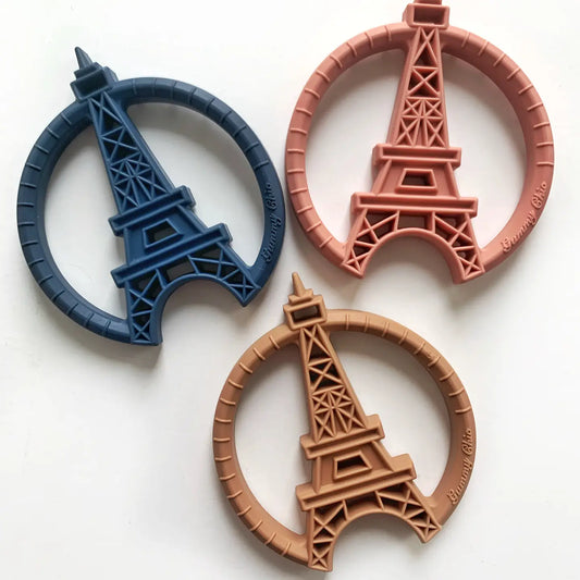 Three silicone teething toys designed to resemble the Eiffel Tower, in blue, pink, and brown colors, displayed against a white background.