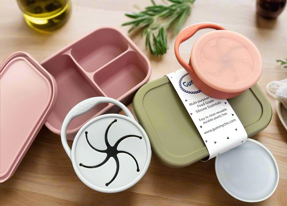 A silicone bento box lunchbox with compartments, along with its lid and additional silicone containers, displayed on a wooden surface.