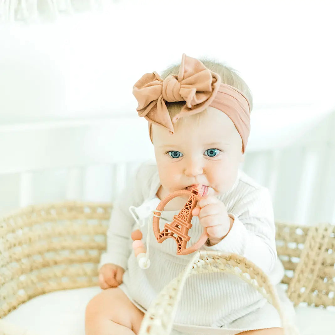 Baby using Paris silicone teething toy with Eiffel Tower design, wearing a cute headband.