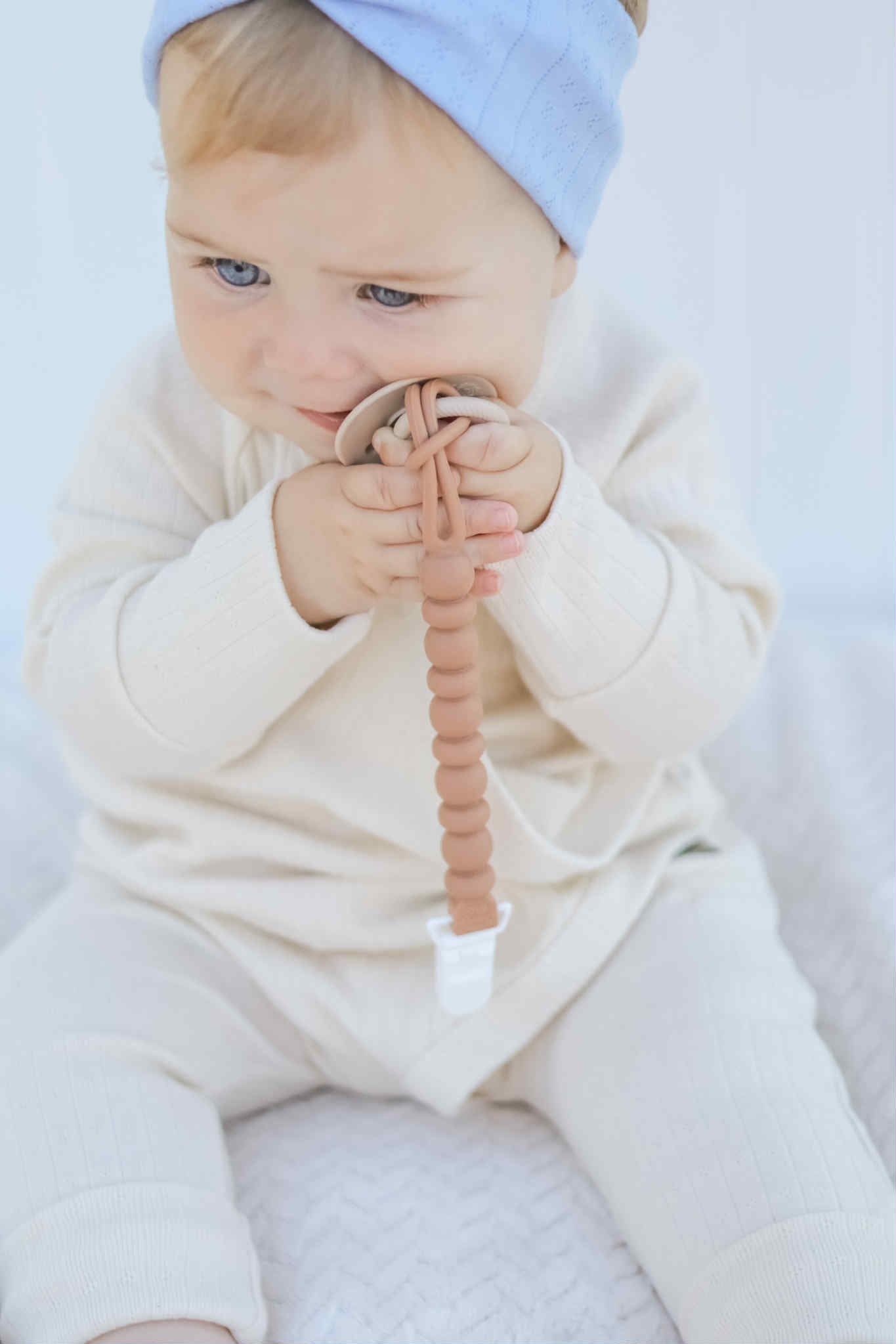 Baby holding a pacifier with a pacifier clip against a white background