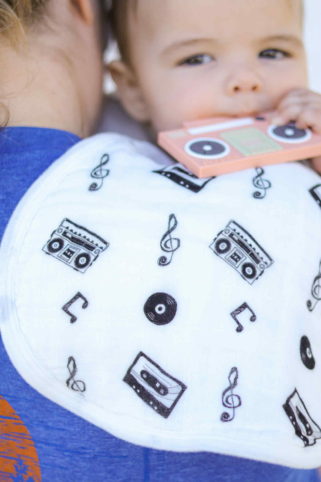 Baby wearing a bib with music-themed patterns, holding a toy.