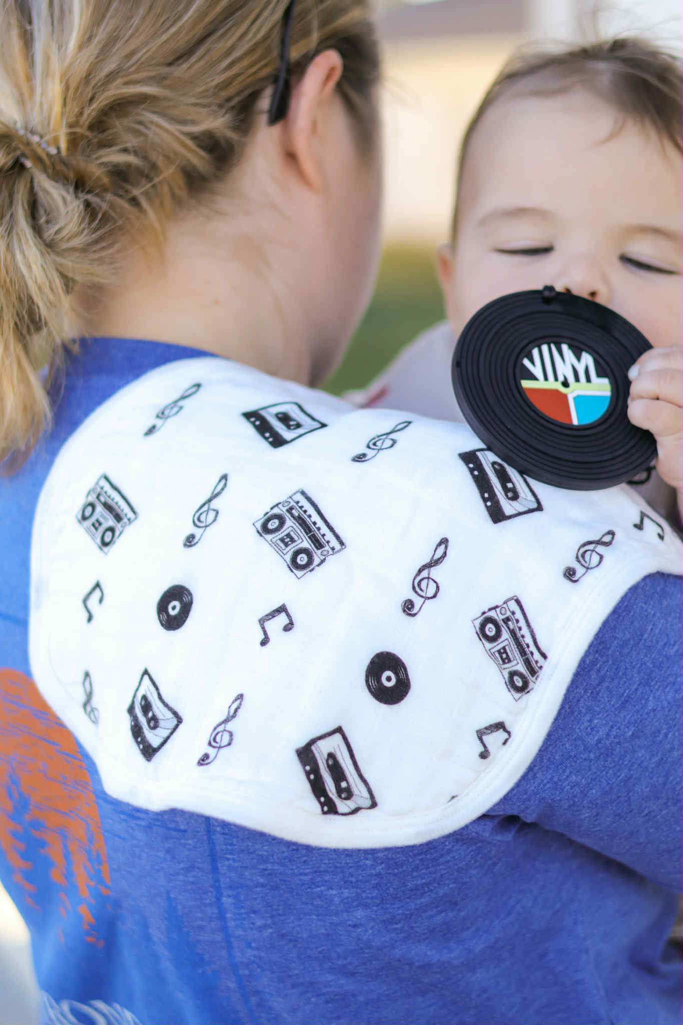 Child teething while being carried by an adult outdoors wearing a burr rag