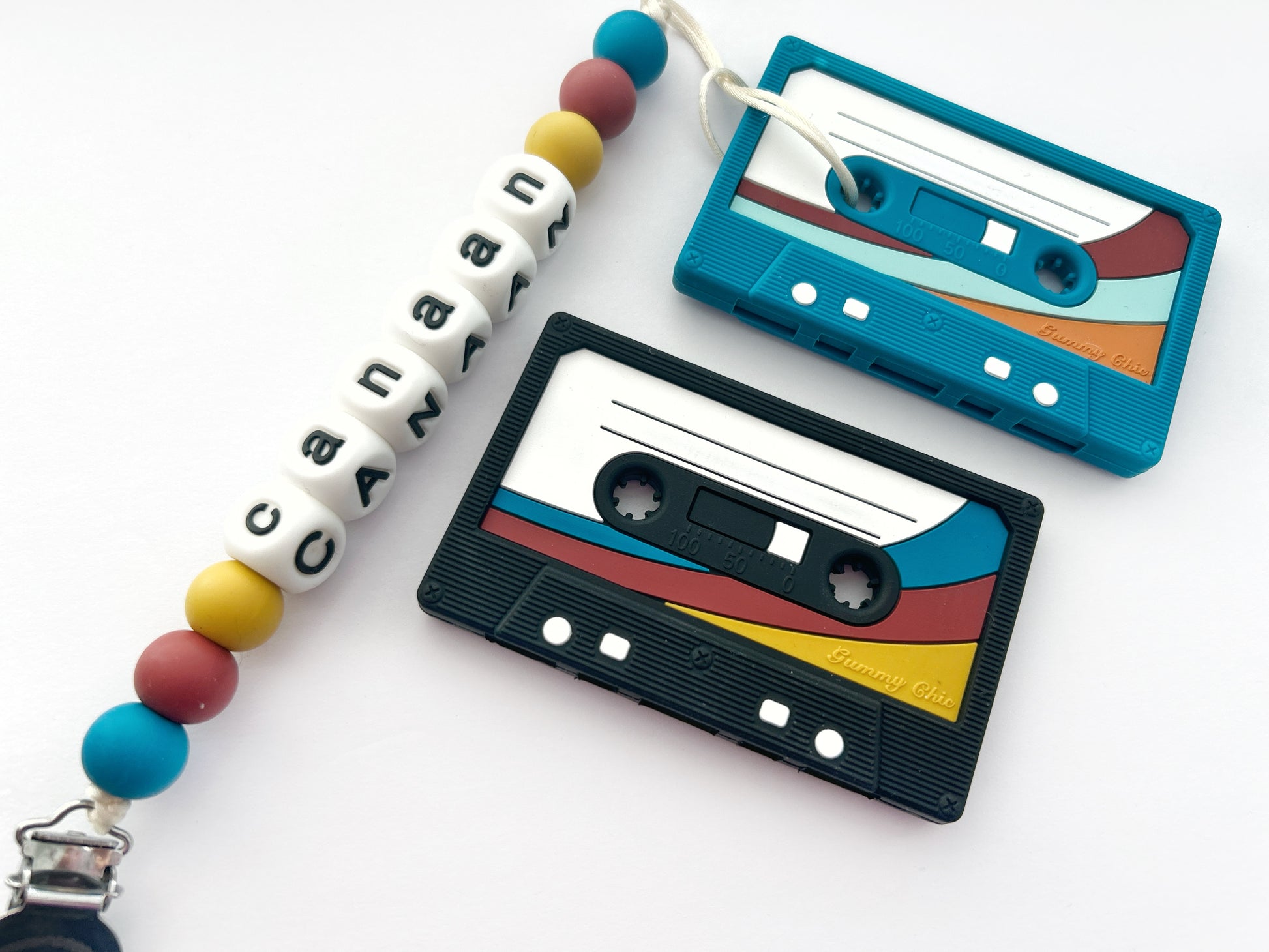 A silicone teether designed to resemble a cassette tape with colorful stripes, attached to a pacifier clip with multicolored beads.