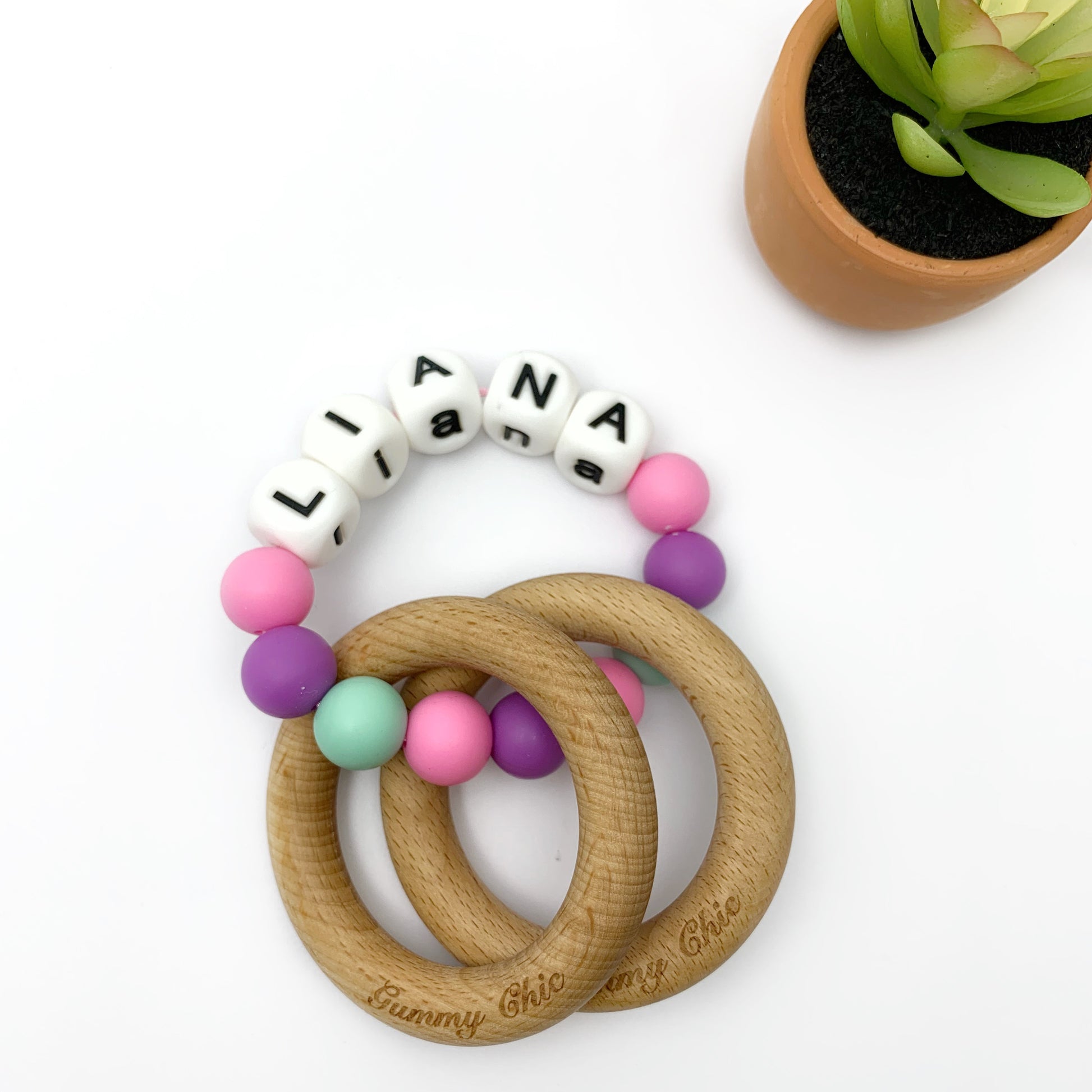 pink mint and purple silicone beads with letter beads forming a girls name and wooden rings.