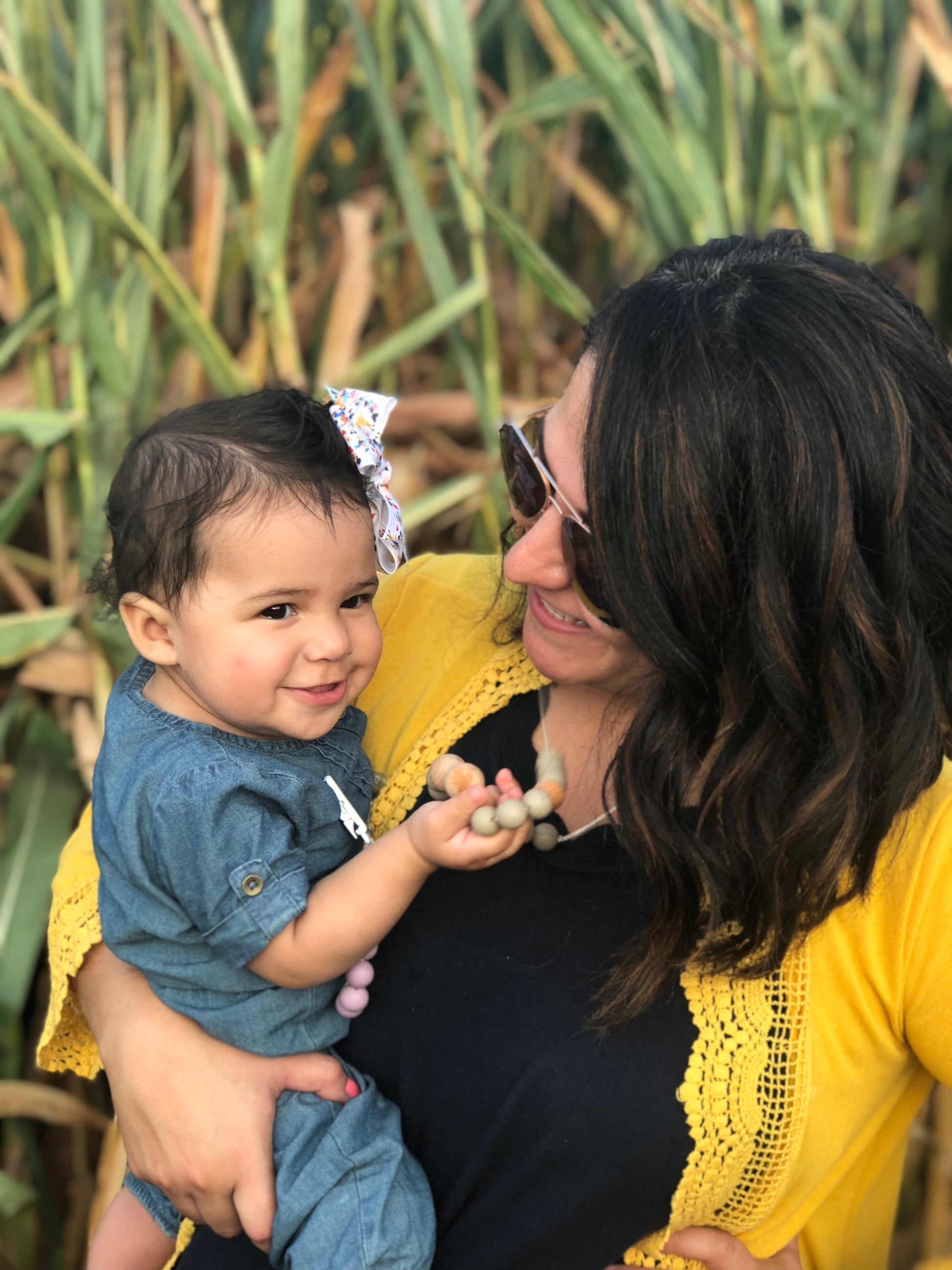 mom is wearing a teething necklace and baby girl is playing with the beads on it.