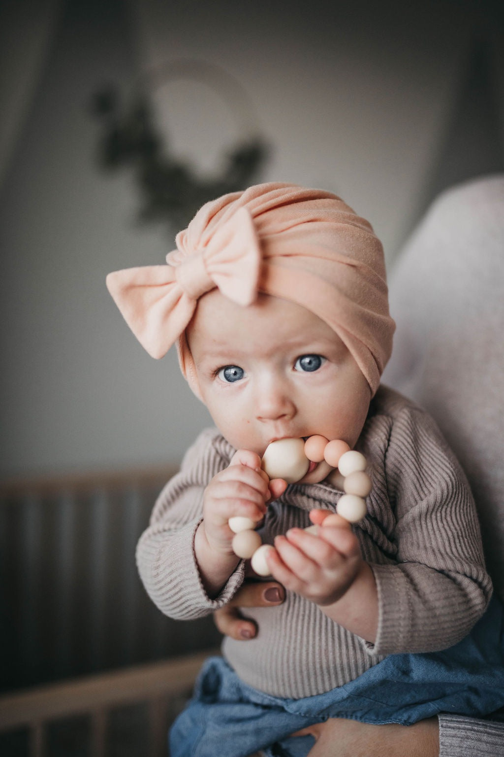 baby girl holding  a teething ring in beige and neutral colored beads