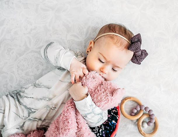 sweet peaceful baby girl eyeing her teether rattle toy and holding a bear