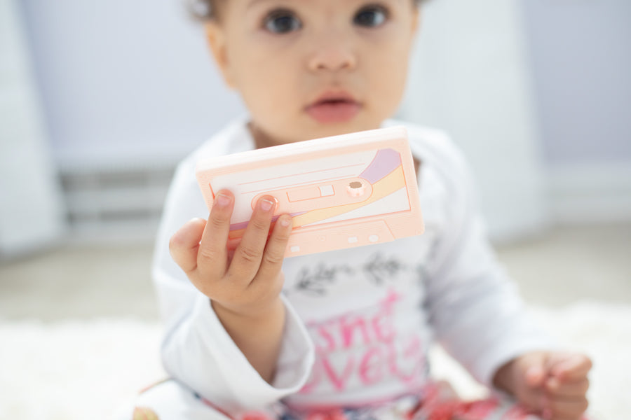 Baby holding a Cassette Mix Tape Teether, showcasing retro 80s and 90s vibes for teething relief.