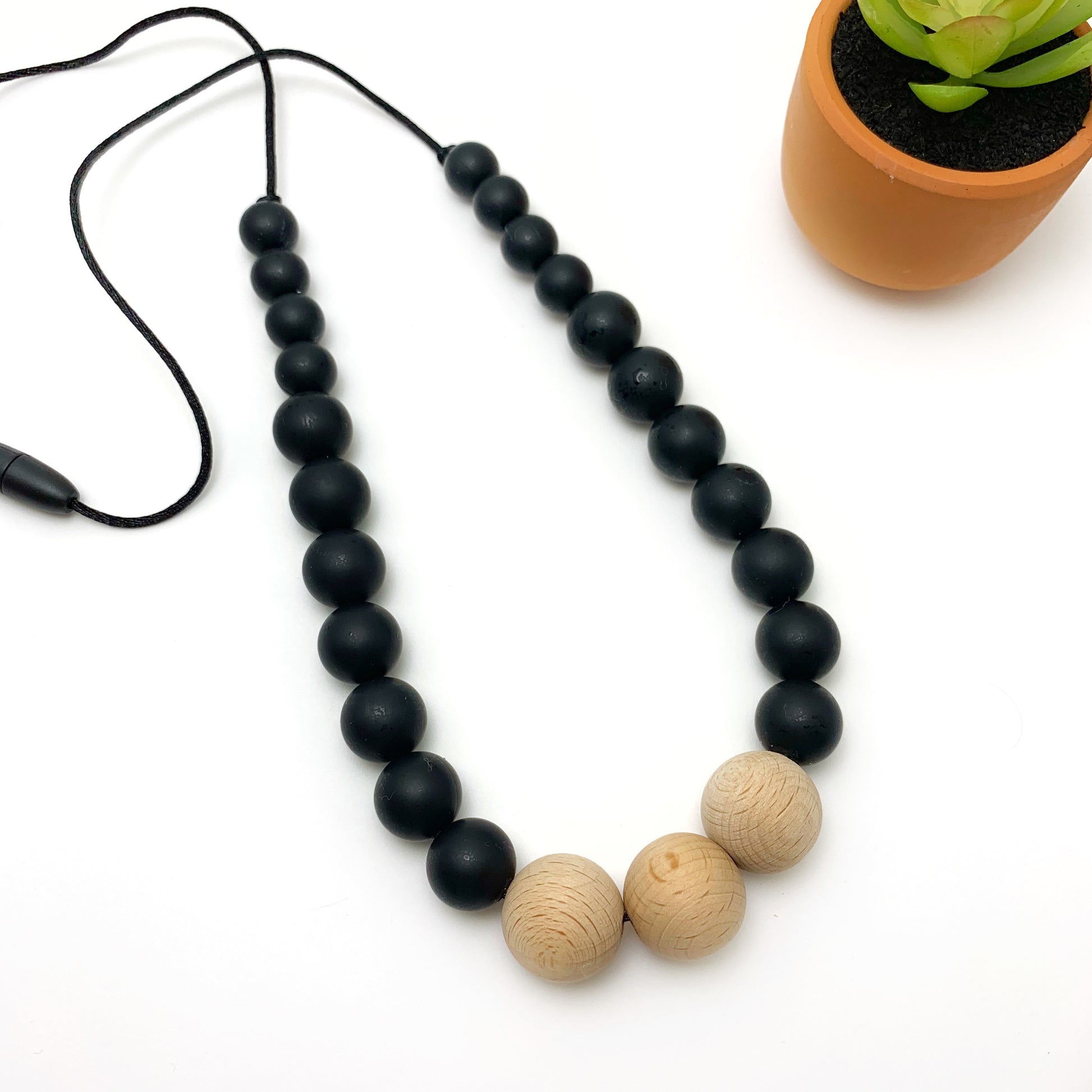 teething necklace for mom in black silicone beads with three wooden beads at the center with a breakaway clasp