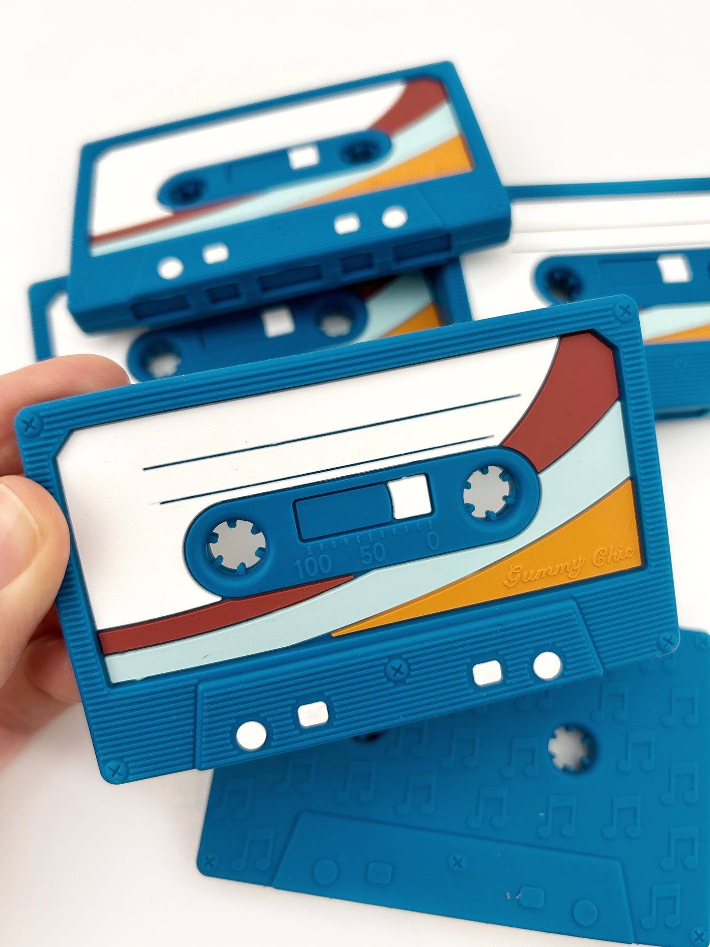 close up of a blue retro mix tape silicone teether with several of the same on the background