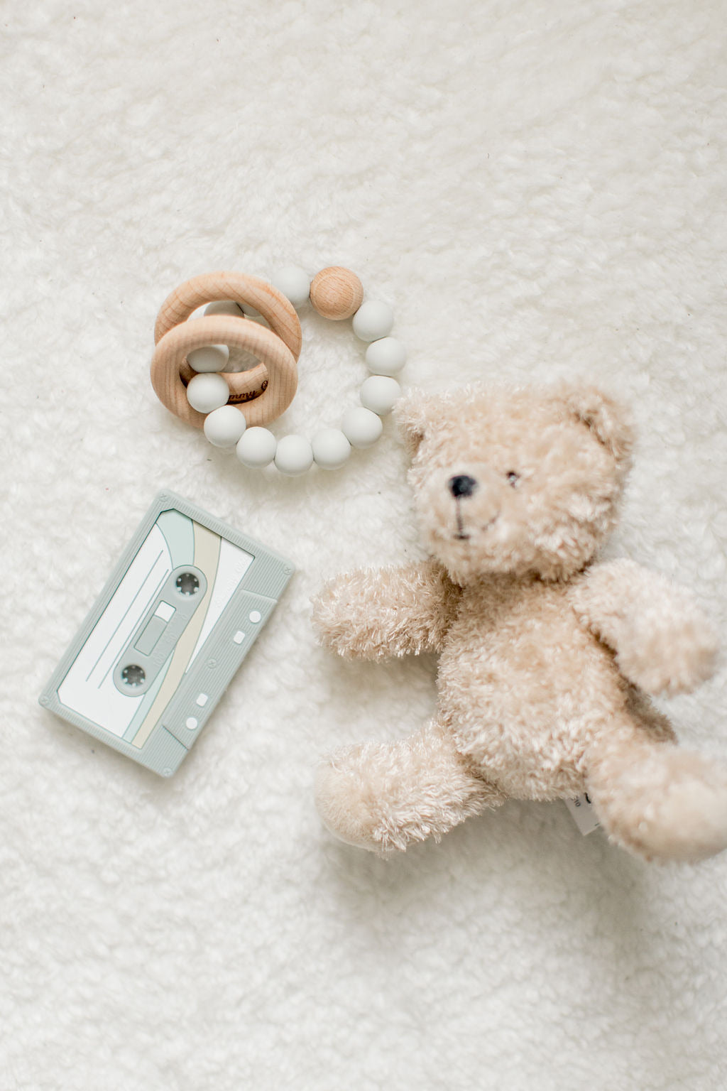 white background, teddy bear, cassette tape teether and a light colored  wood and silicone teether
