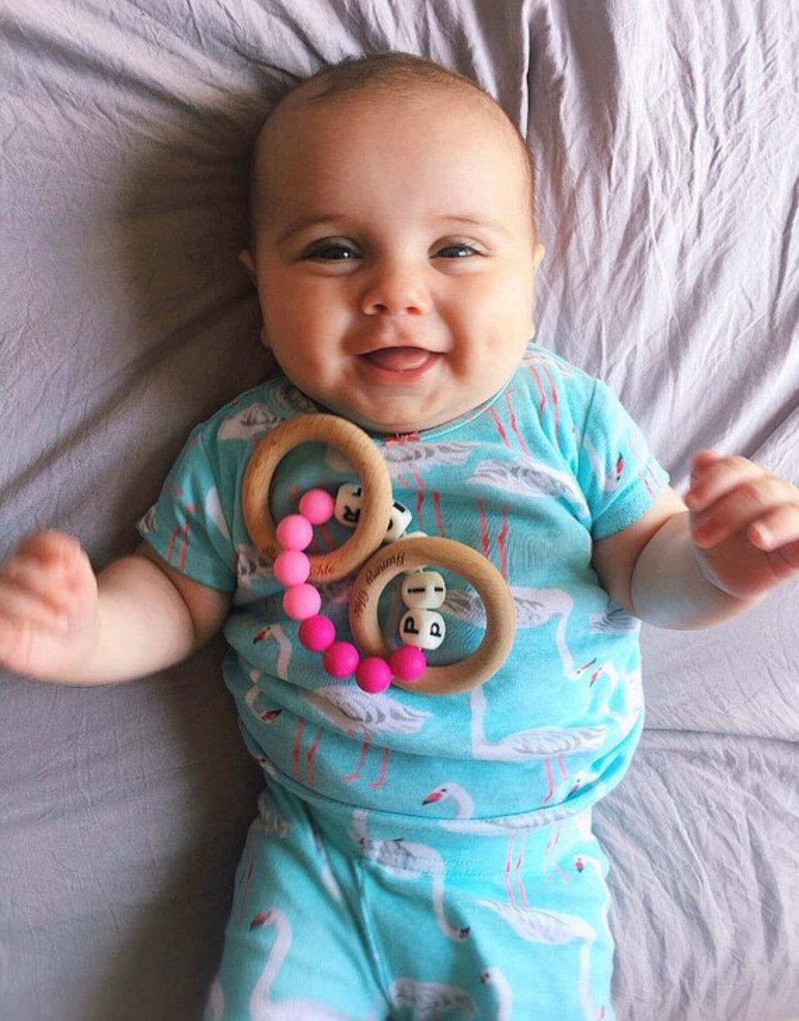 baby girl laying down in her bed with her personalized teether on her chest