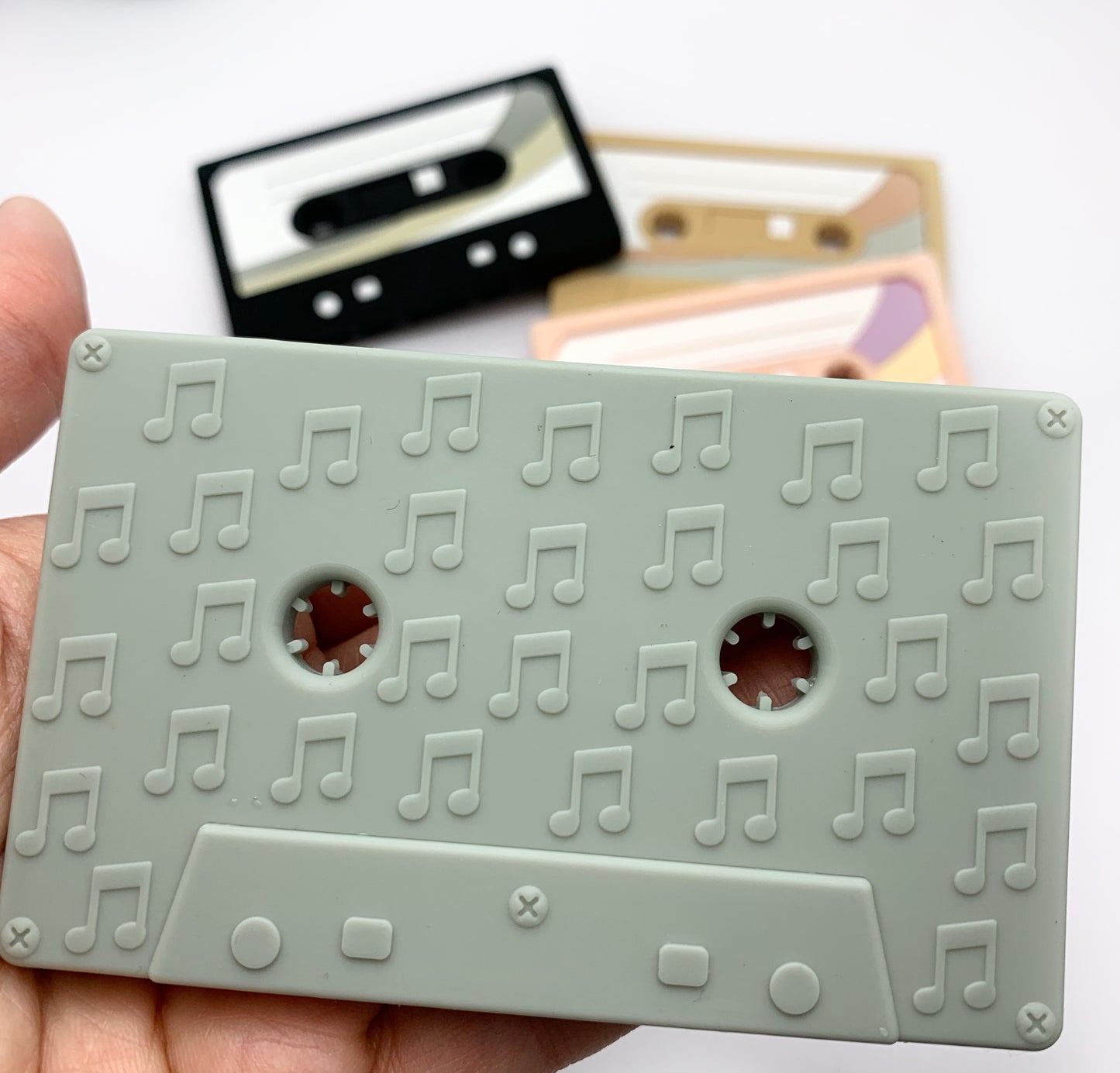 close up of a grey cassette teething toy with musical notes on the back