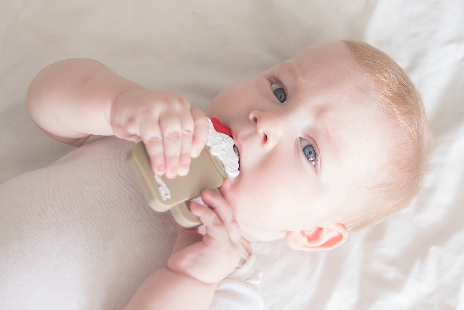 Baby holding a teether in the shape of a coffee or chocolate milkshake teether with a red cherry and white cream on top.