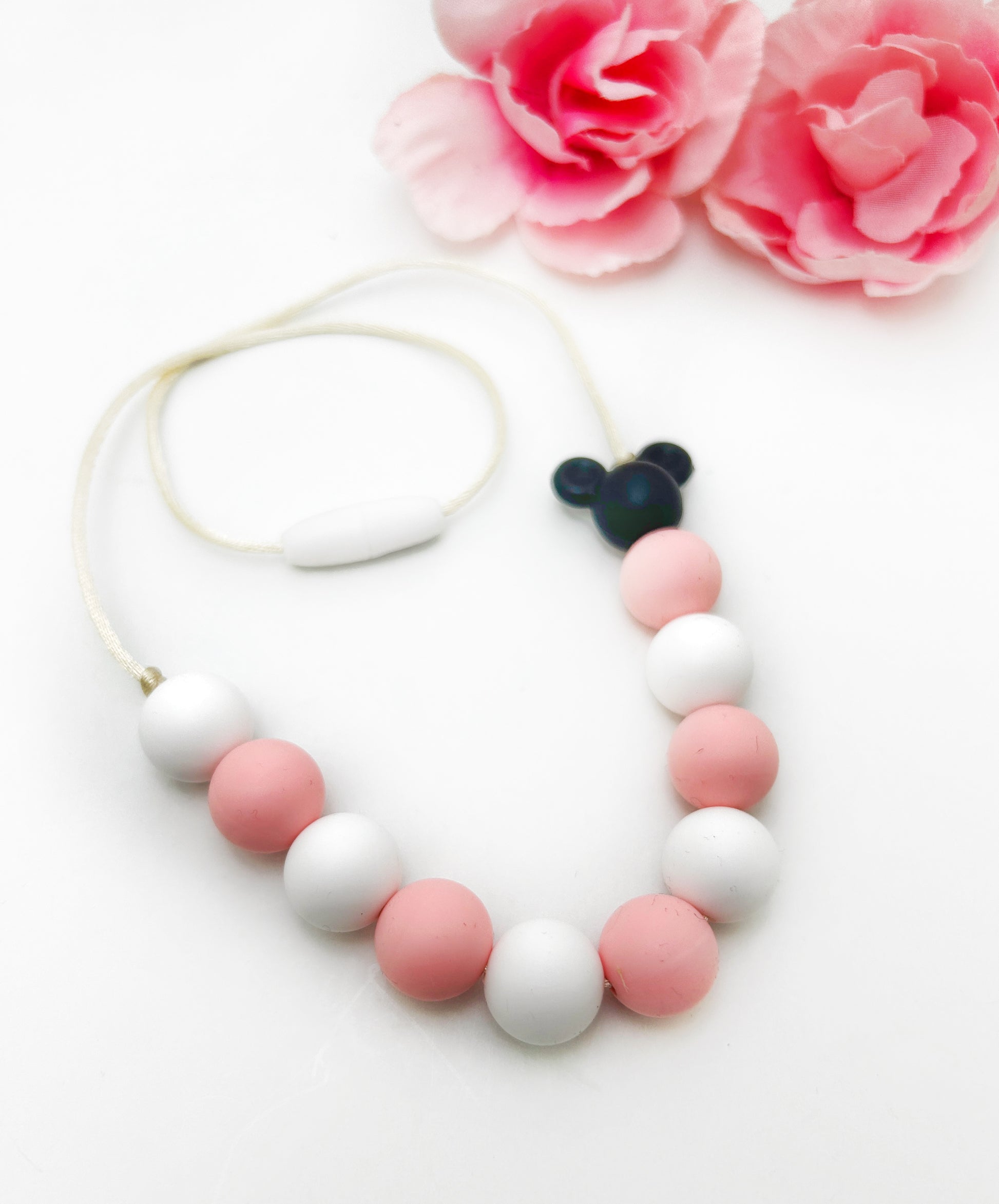 Necklace with pink and white beads and a black pendant on a white background with pink flowers.