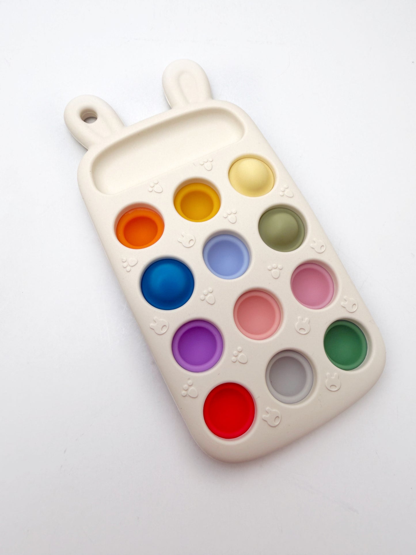 An off-white silicone baby teething toy or ice cube tray with bunny ears at the top, featuring multiple colorful circular wells in orange, yellow, blue, green, pink, purple, red, and gray, set against a plain white background.