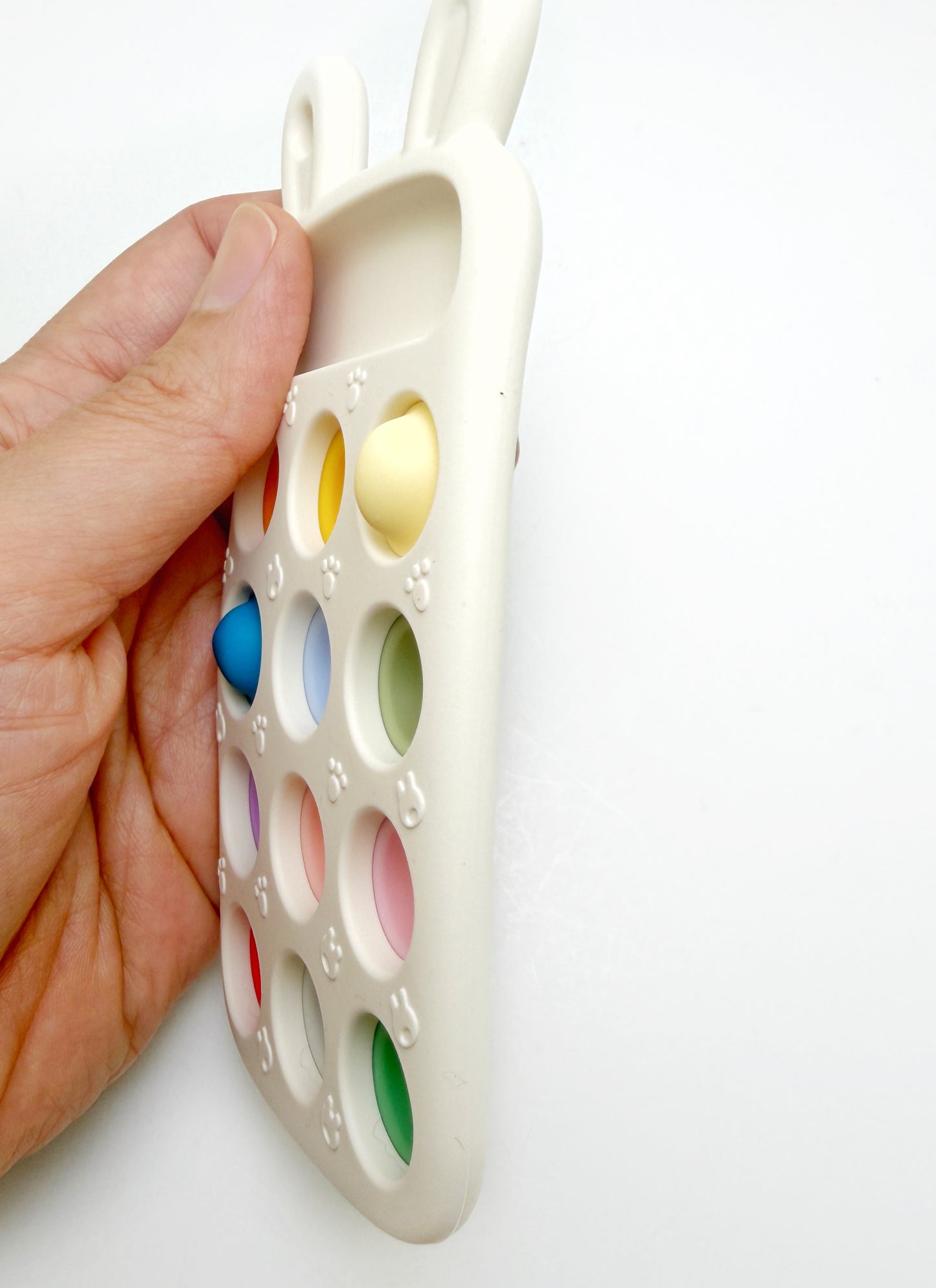 A hand holding a white silicone baby teething toy shaped like a bunny head with colorful circular inserts, shown against a plain white background.