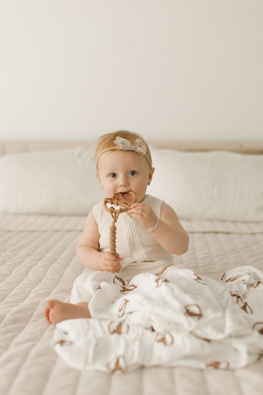 A baby sitting on a bed with a white Paris themed receiving blanket with gold accents around the edges.