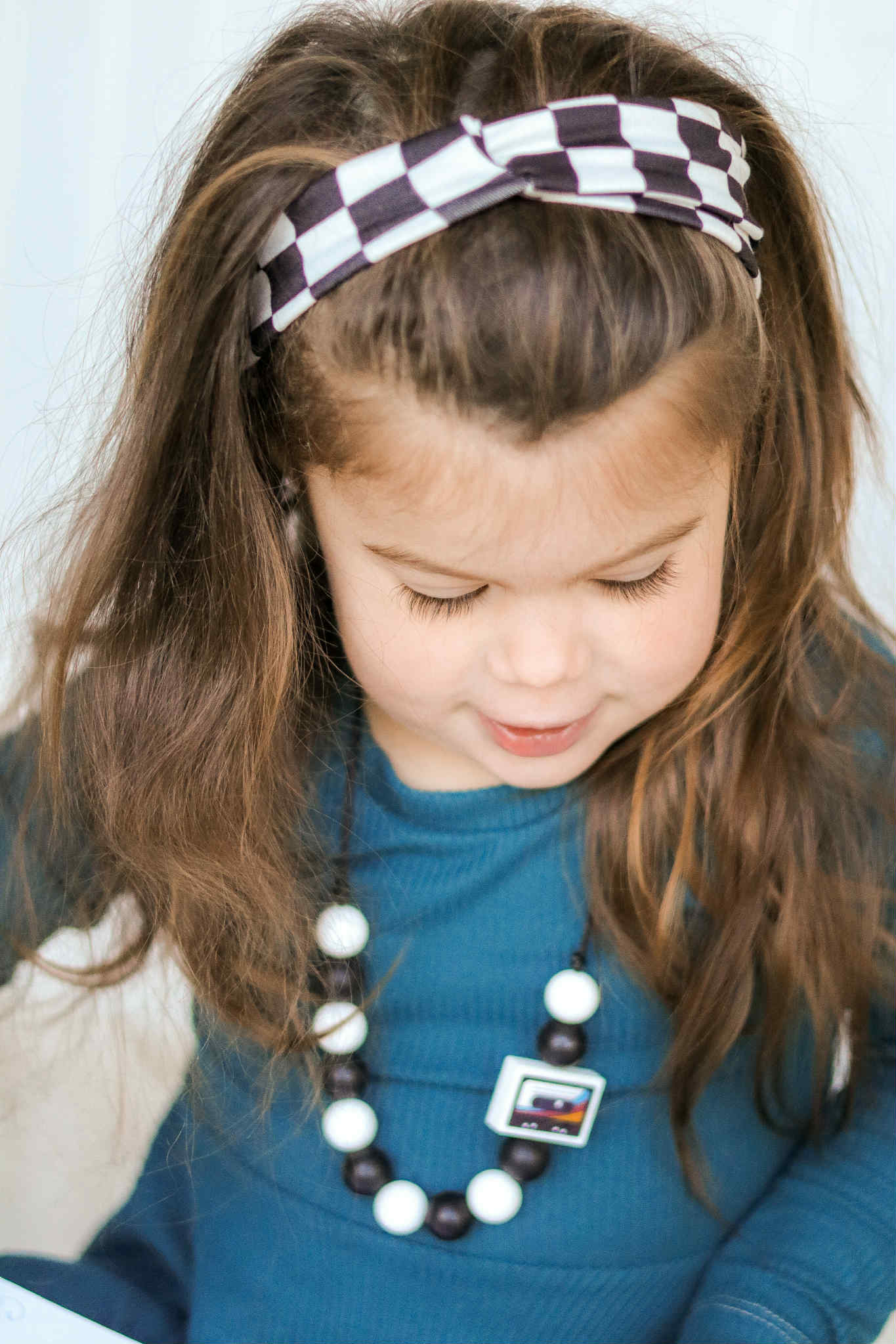 Child wearing a blue shirt and checkered headband, looking down.
