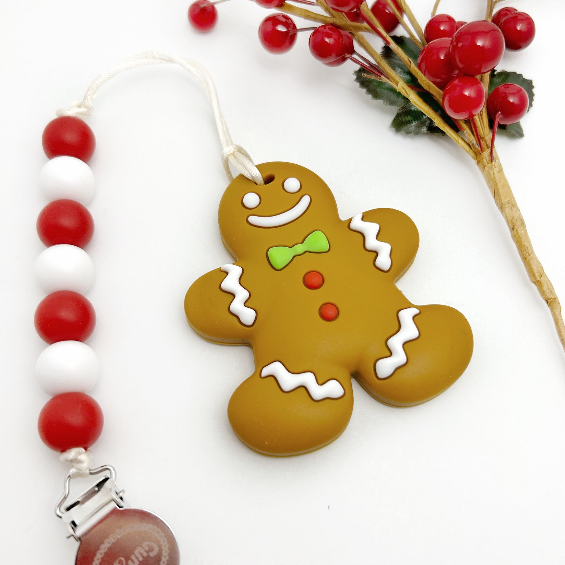 A festive gingerbread man-shaped teether with red and white beads on a chain, displayed next to Christmas decorations.