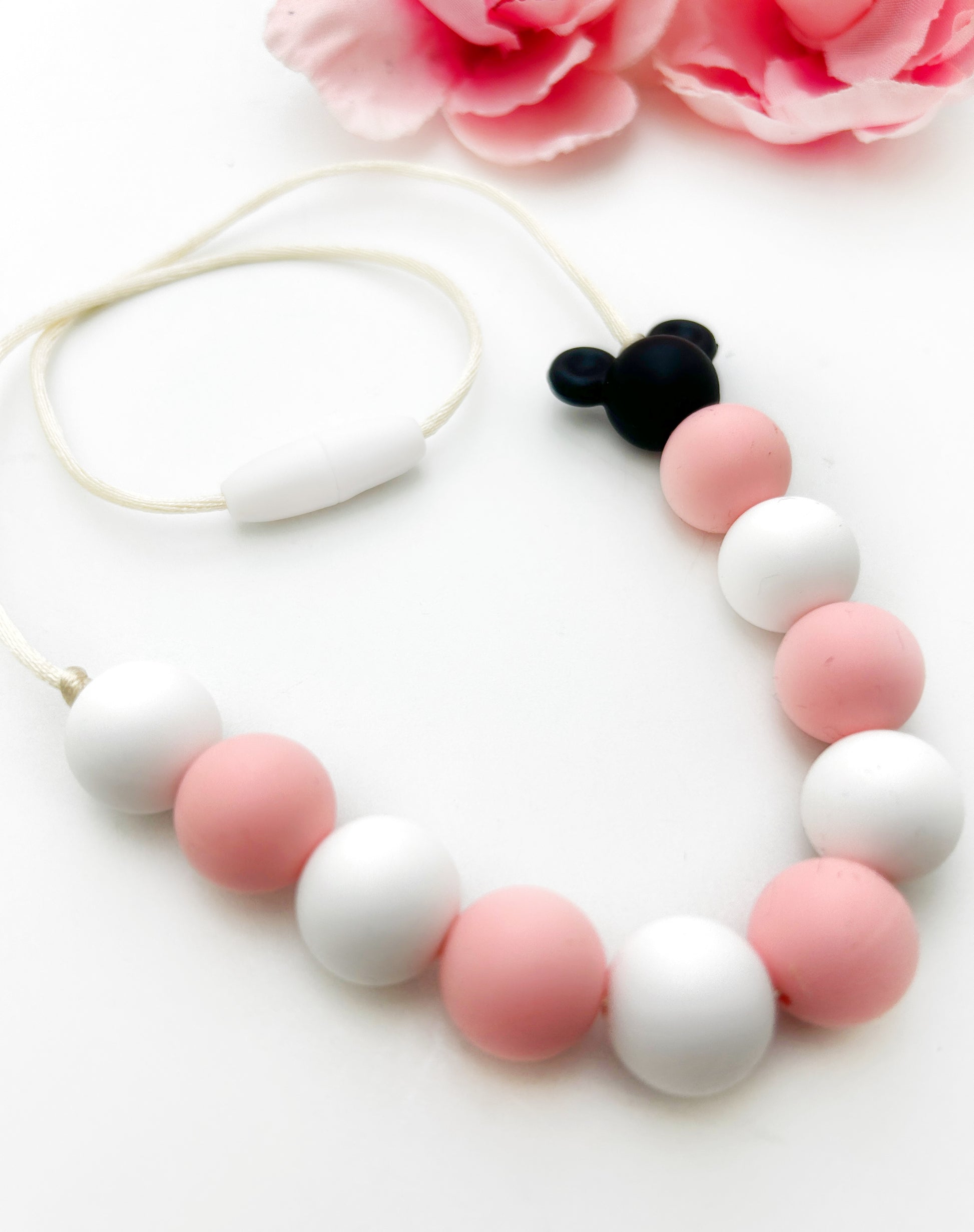 Necklace with pink and white beads and a black and white pendant on a white background with pink flowers.
