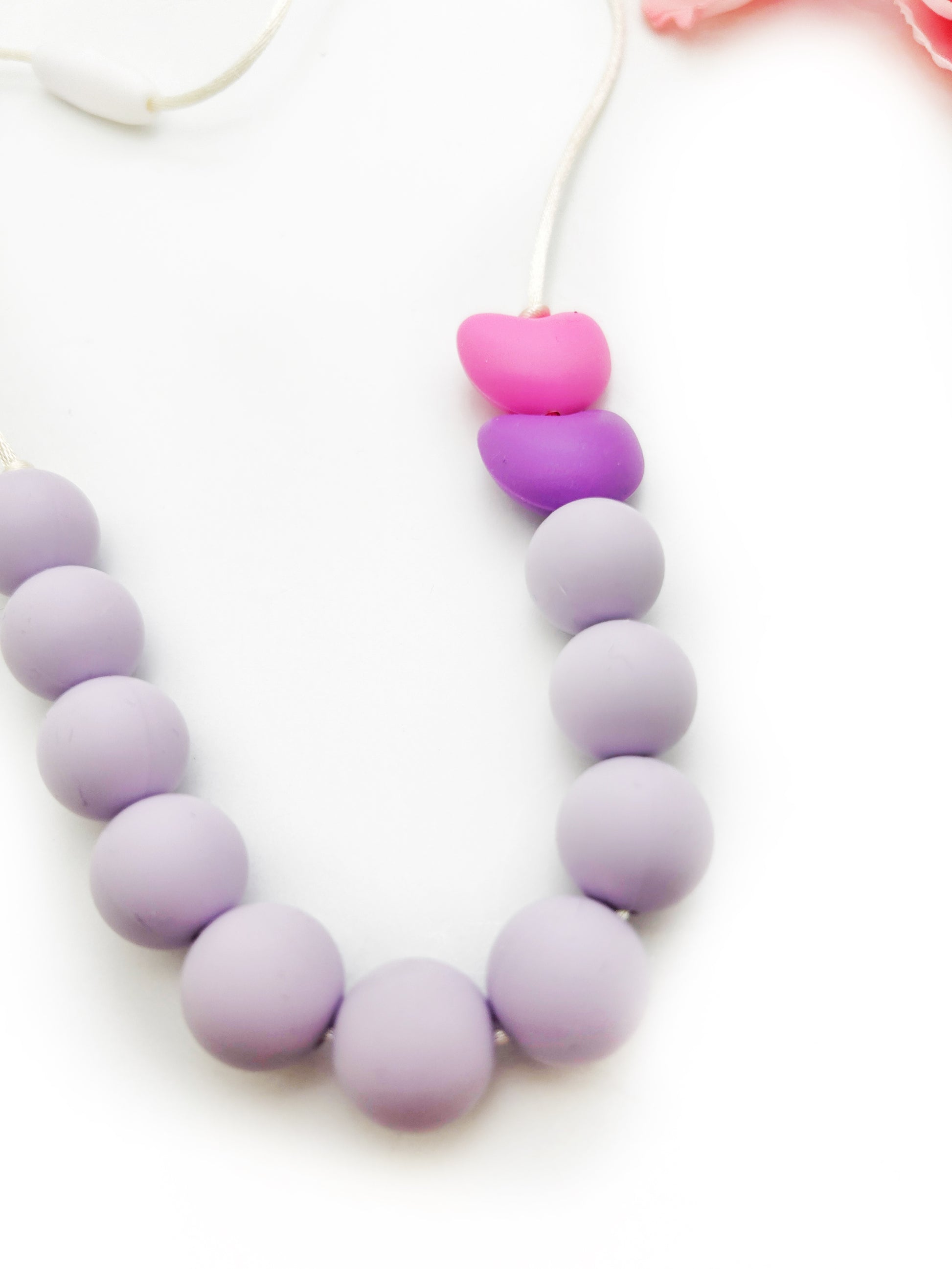 Necklace with purple beads and a pink heart-shaped charm on a white background