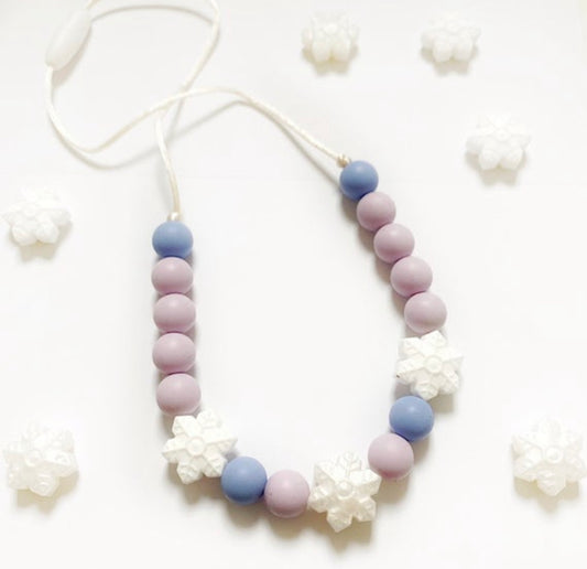 A necklace with purple, blue, and white beads, featuring white flower-shaped charms, displayed against a white background with additional white flowers.