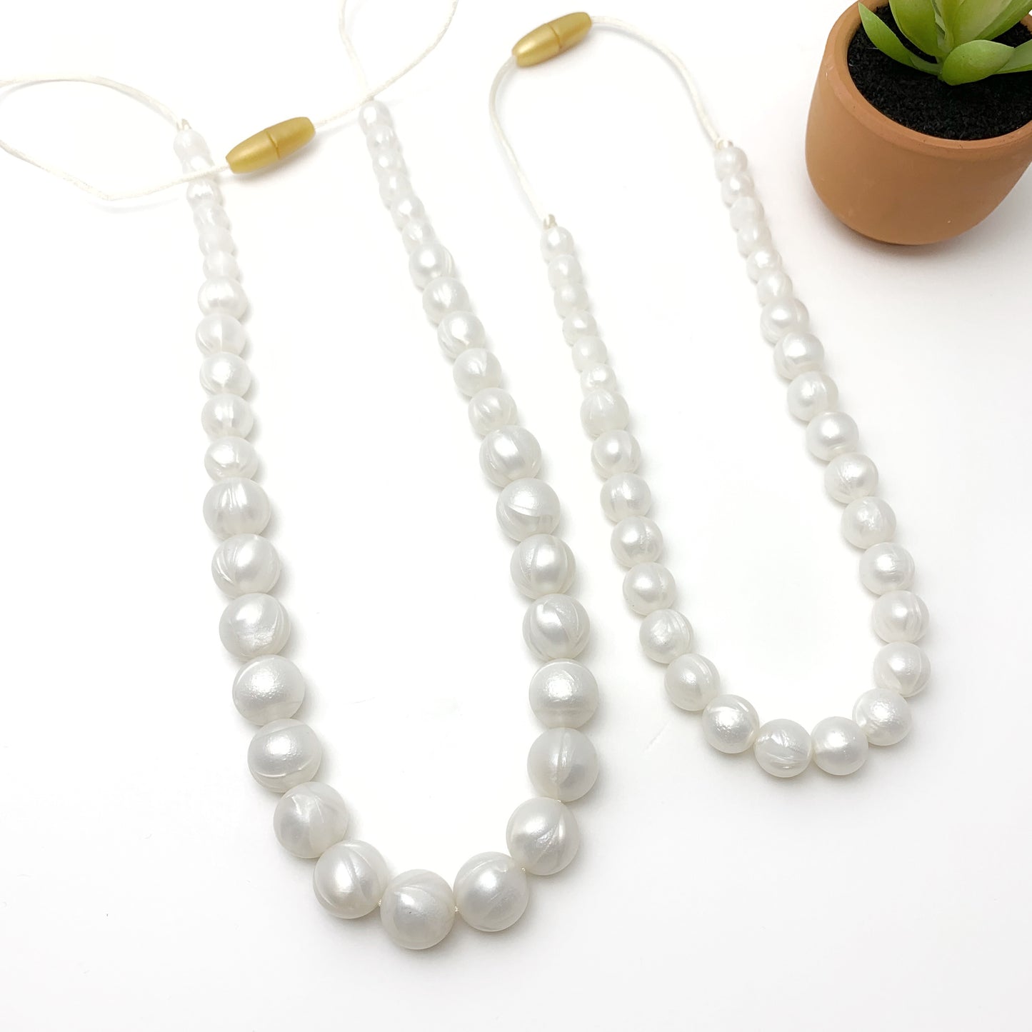 Pearl necklace on a white background with a small plant pot in the corner